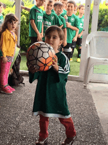 a little girl holding a soccer ball in front of a group of children wearing green shirts that say ' champions '