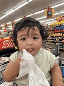 a baby is sitting in a shopping cart in front of a sign that says " sale "