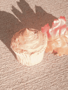 a cupcake sits on a concrete surface next to a fake leaf