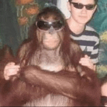 a man and a monkey are posing for a picture . the monkey is wearing sunglasses .