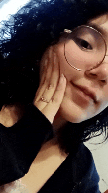 a woman wearing glasses and a ring on her finger touches her face