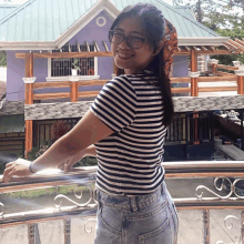 a woman wearing glasses and a striped shirt stands on a balcony