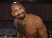 a shirtless man with a tattoo on his chest is smiling in a kitchen