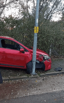 a red car that has crashed into a pole with a yellow sign that says danger