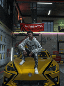 a man sits on the hood of a yellow car in a garage