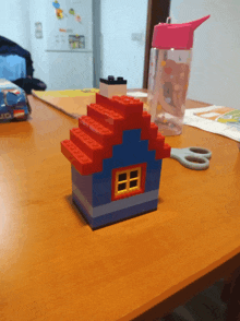 a small lego house sits on a table next to a pair of scissors and a water bottle