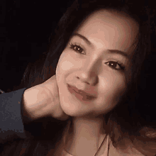 a close up of a woman 's face with her hand on her neck and a smile on her face .