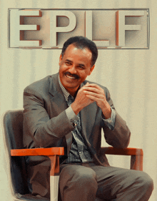 a man in a suit sits in a chair with the word eplf behind him