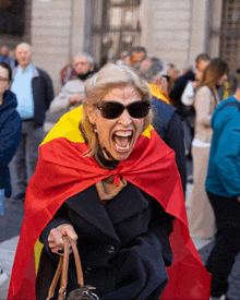 a woman wearing sunglasses and a red and yellow cape with a spanish flag on it