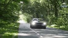 a car is driving down a road with trees on both sides and a sign in the background that says ' aachen '