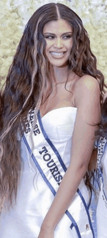 a woman with long hair is wearing a white dress and a sash that says tours .