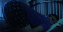 a man in a blue shirt is sleeping on a bed with white stars on his shorts