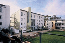 a man is sitting on a balcony reading a book in front of a large apartment building .