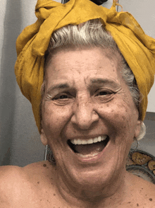 an elderly woman wearing a yellow scarf on her head smiles for the camera