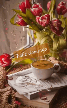 a cup of coffee sits on top of a book next to a vase of flowers and the words feliz domingo