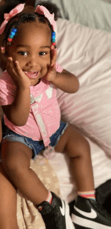 a baby girl wearing a pink shirt and shorts is sitting on a bed