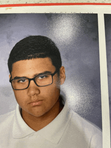 a young man wearing glasses and a white polo shirt looks at the camera