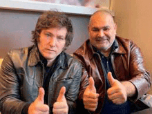 two men in leather jackets are giving each other thumbs up .