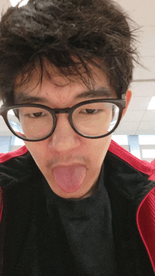 a young man wearing glasses and a red jacket sticks his tongue out