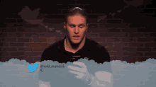 a man in a black shirt is holding a cell phone in front of a twitter banner