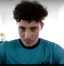 a young man with curly hair is wearing a blue shirt with the word fin on it