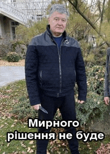 a man in a black jacket is holding a knife and standing in a park .