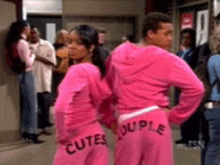 a man and a woman are standing next to each other wearing pink sweatpants that say cutes couple on them .