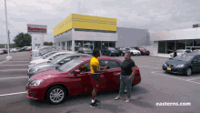 a man in a yellow jersey is shaking hands with a woman in a red car in front of a easterns dealership