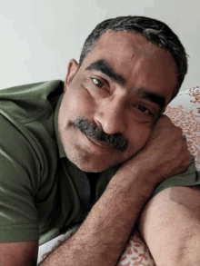 a man with a mustache rests his head on his arm and smiles