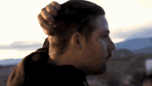 a man is holding his hair in a bun while standing in front of mountains .