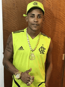 a young man wearing a yellow adidas shirt and a yellow hat is giving a thumbs up