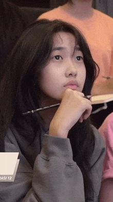 a young girl is sitting in a classroom with a pen in her hand and looking at the camera .