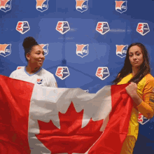 two women holding a canadian flag in front of a wall with logos for the us women 's soccer association