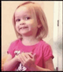 a little girl in a pink shirt is clapping her hands in a room .