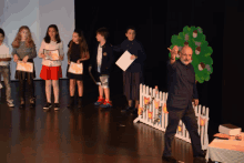 a group of children are standing on a stage with a man standing in front of them