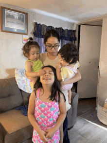 a woman is holding three children in her arms and one of them is wearing a pink tank top