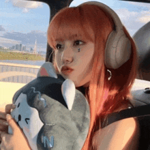 a girl with red hair is wearing headphones and holding a stuffed animal in her car .