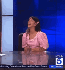 a woman in a pink and white striped shirt is sitting at a table with a glass of water and laughing .