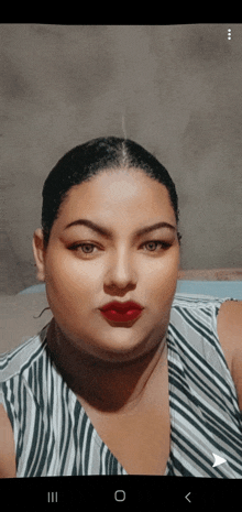 a woman wearing a striped shirt and red lipstick is looking at the camera