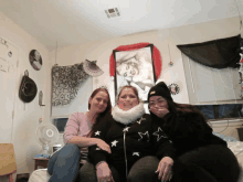 three women are posing for a picture in front of a wall with a picture of a woman