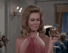 a woman in a pink dress is holding a glass of whiskey in a room .