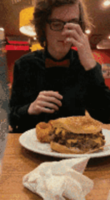 a man in a bow tie is sitting at a table with a plate of food in front of him