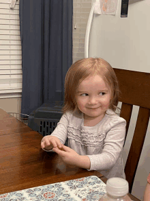 a little girl is sitting at a table with a bottle of water