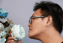 a man wearing glasses smells a flower in his hand