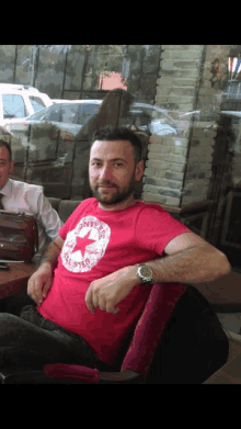 a man wearing a red converse shirt is sitting in a chair