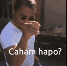 a man wearing sunglasses and a white shirt is smoking a cigarette and says caham hapo .