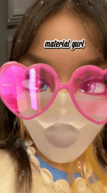 a girl wearing pink heart shaped glasses has a sticker on her forehead that reads material girl