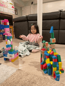 a little girl sits on the floor playing with blocks including a stack of blocks with the letter a on it