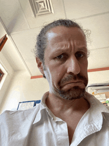 a man with a beard wearing a white shirt making a face