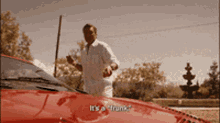 a man standing next to a red car with the words " it 's a trunk " on the hood